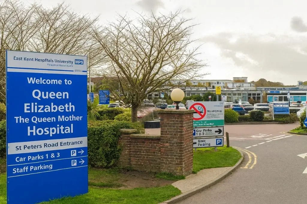Hospital entrance sign with nearby cars and parking area.