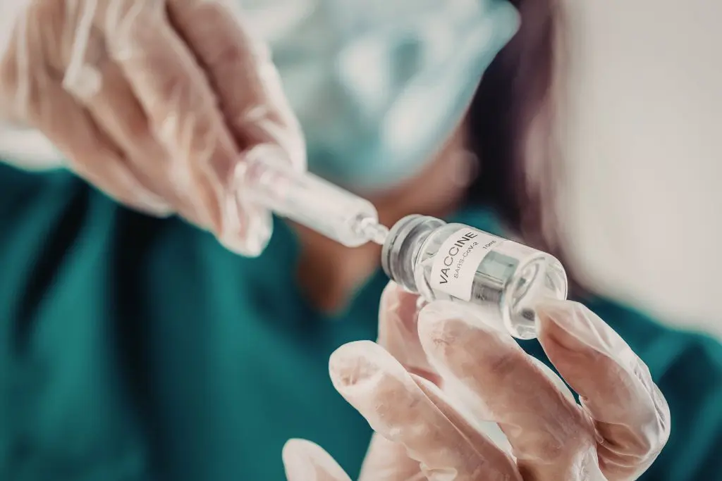Healthcare worker in gloves and a mask drawing a dose from a vaccine vial into a syringe