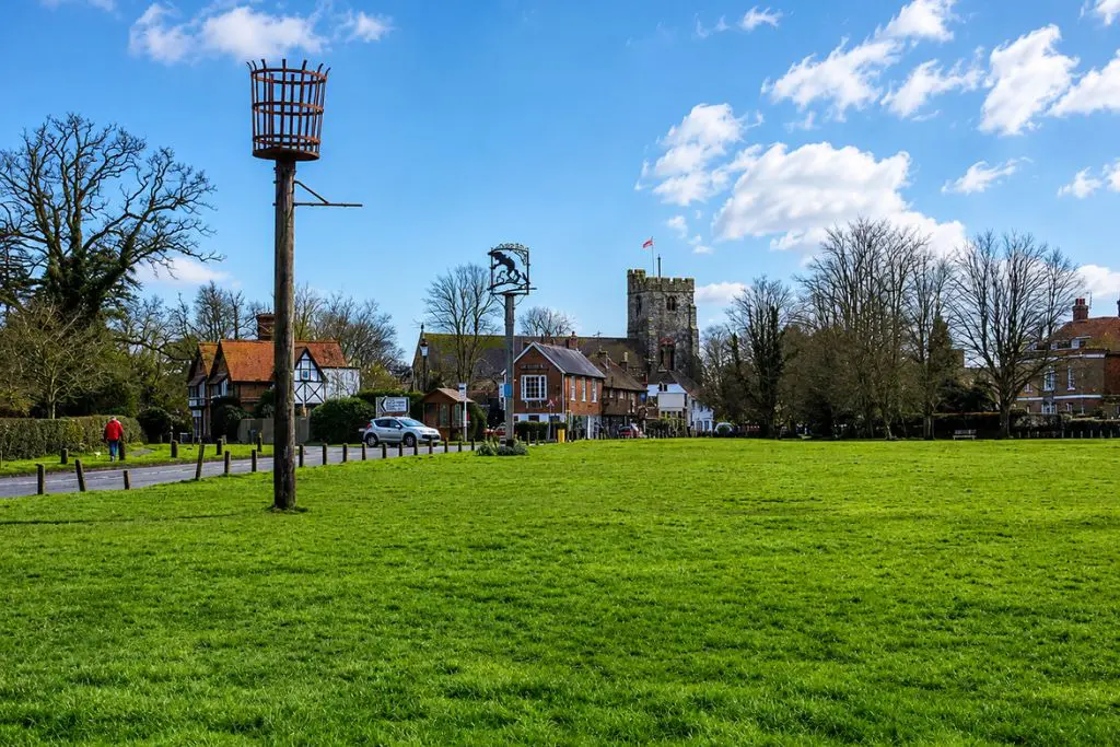 Hawkhurst village green with a wooden beacon, a central sign post, and a stone church tower in the background.